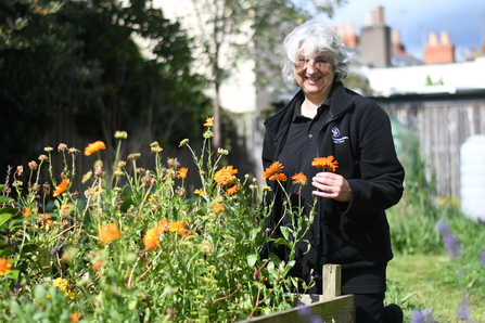 Frances smiling at the camera, in a garden with wildflowers.